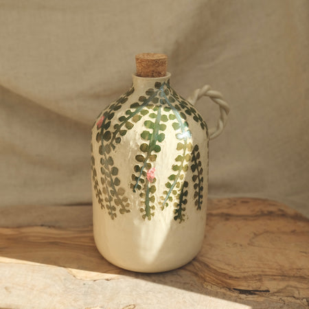 Ceramic bottle with floral design and cork stopper on a wooden surface